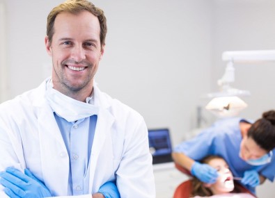 Dentista sorrindo com paciente e outra dentista no fundo