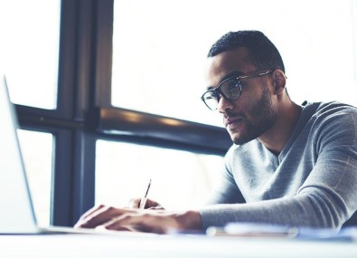 Homem escrevendo e olhando o computador