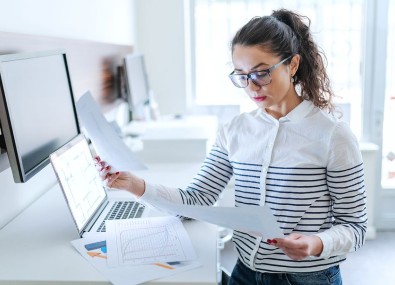 Mulher usando computador e verificando papéis