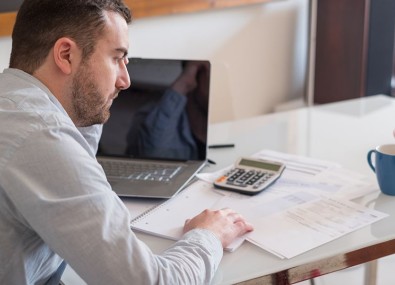 Homem com mão na cabeça com contas e calculadora na mesa