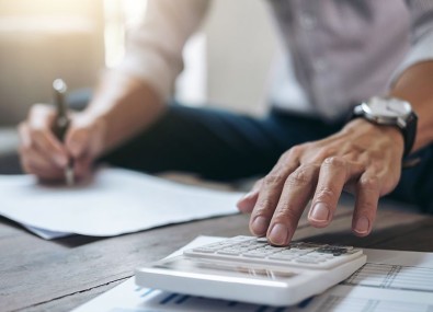 Homem escrevendo no papel e usando calculadora