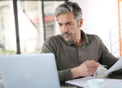 Homem olhando o computador e segurando papel